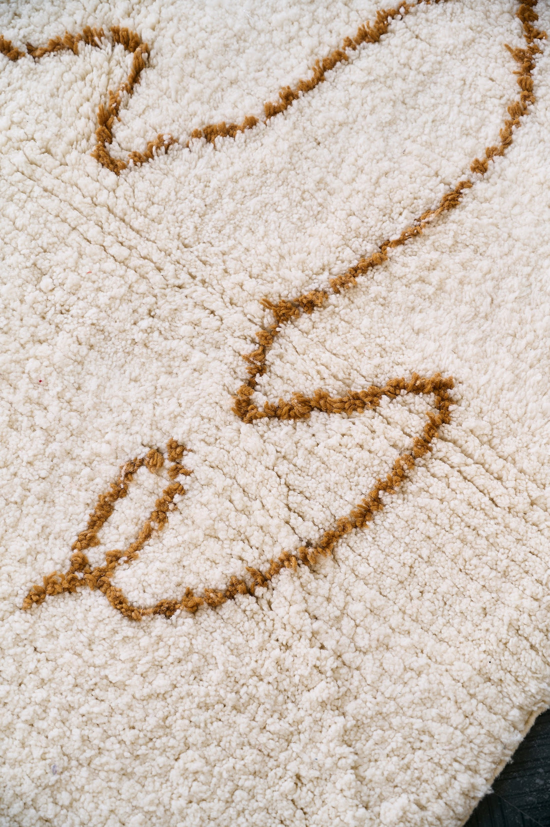 Beige rug with a brown abstract camel design on a gray floor, next to a white table with green fruits.